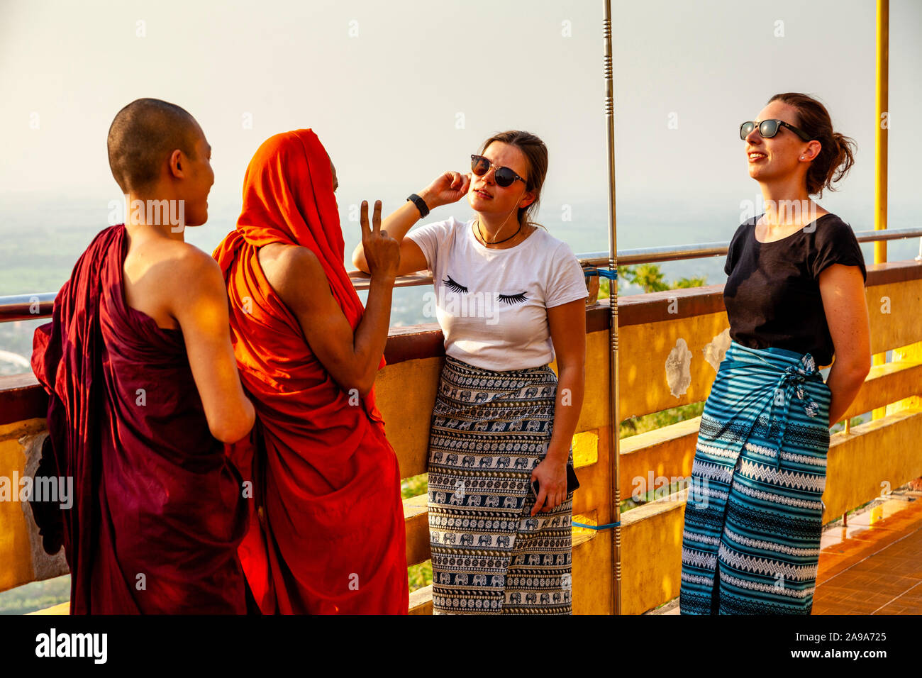 Zwei weibliche Touristen im Gespräch mit einer Gruppe von buddhistischen Mönchen, Su Taung Pyae Pagode, Mandalay Hill, Mandalay, Myanmar. Stockfoto