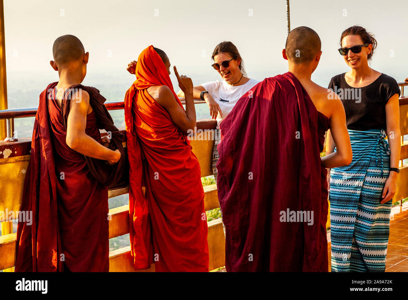 Zwei weibliche Touristen im Gespräch mit einer Gruppe von buddhistischen Mönchen, Su Taung Pyae Pagode, Mandalay Hill, Mandalay, Myanmar. Stockfoto