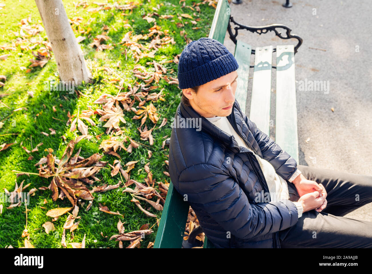 Eher ernsthaften jungen Mann in eine Kappe auf einer Bank an einem sonnigen Herbsttag. Stockfoto