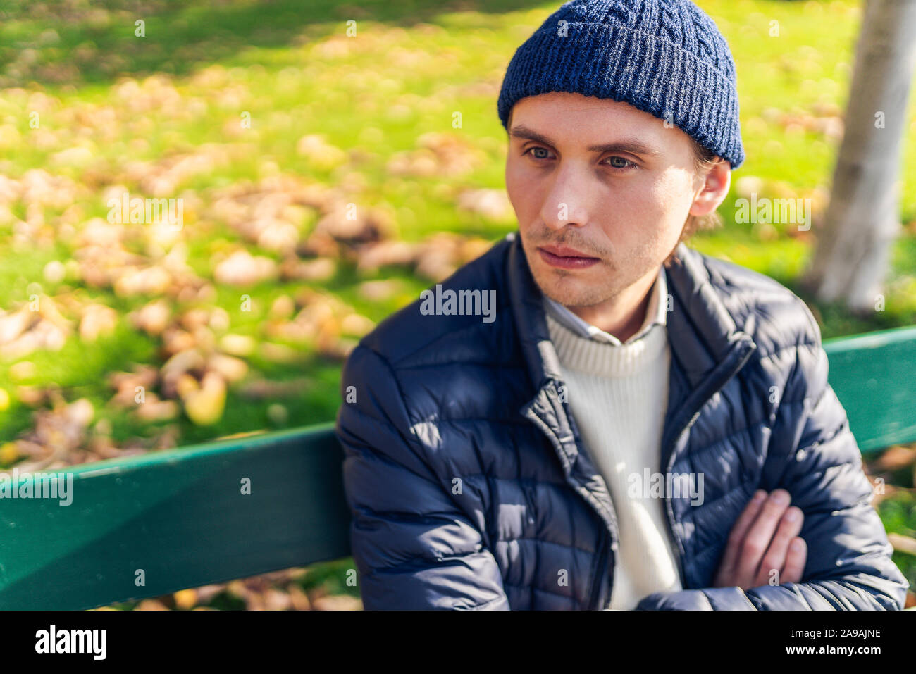 Eher ernsthaften jungen Mann in eine Kappe auf einer Bank an einem sonnigen Herbsttag. Stockfoto