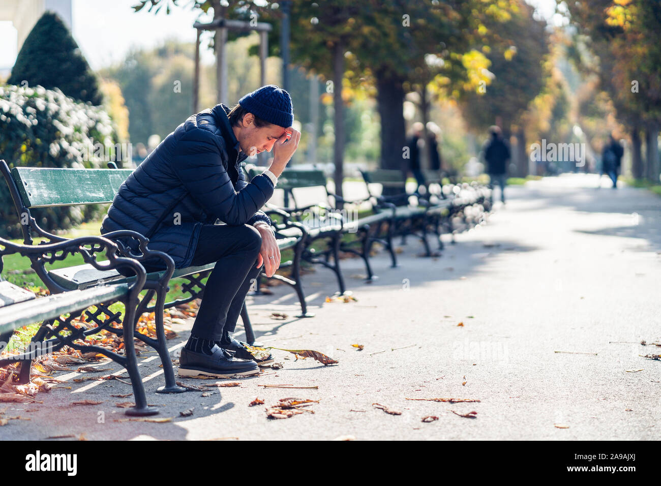 Junge besorgt, der Mensch ist in seinem Gesicht. Er sitzt auf einer Bank während der sonnigen Herbsttag. Stockfoto