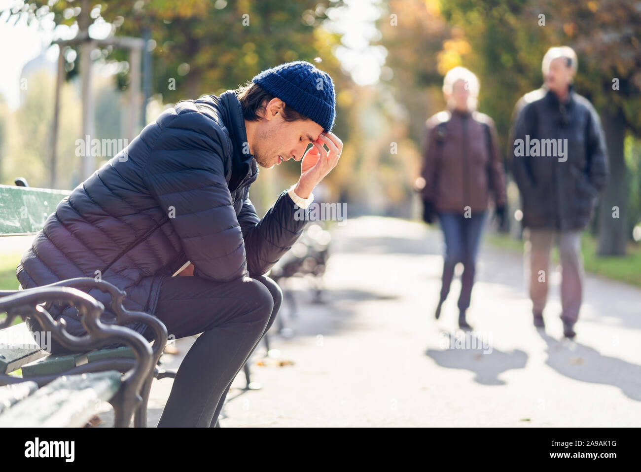 Junge besorgt, der Mensch ist in seinem Gesicht. Er sitzt auf einer Bank während der sonnigen Herbsttag. Die laufen im Hintergrund. Stockfoto