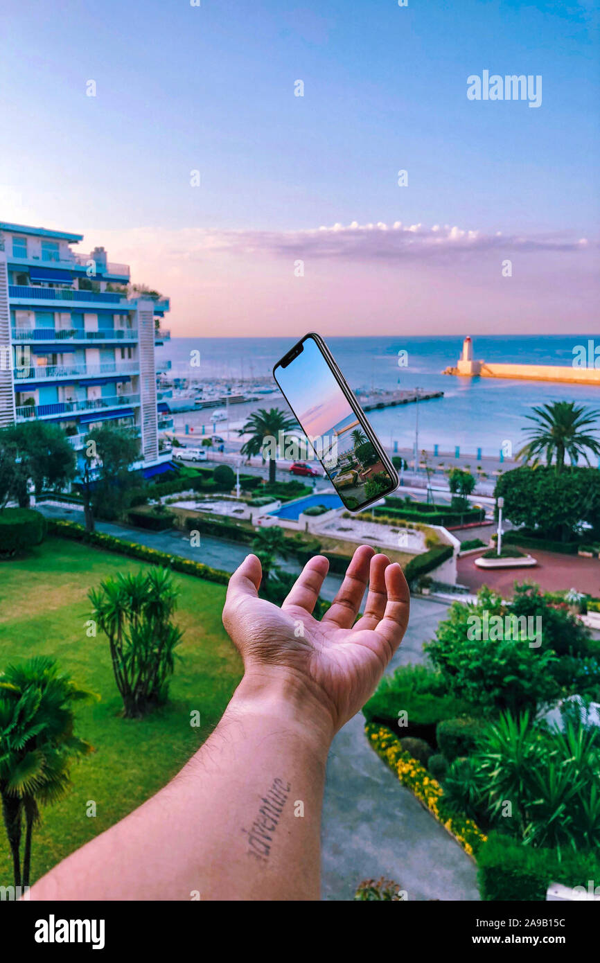 Männliche Hand werfen Sie ein Mobiltelefon mit Hintergrund von Nizza, Mittelmeer Stockfoto