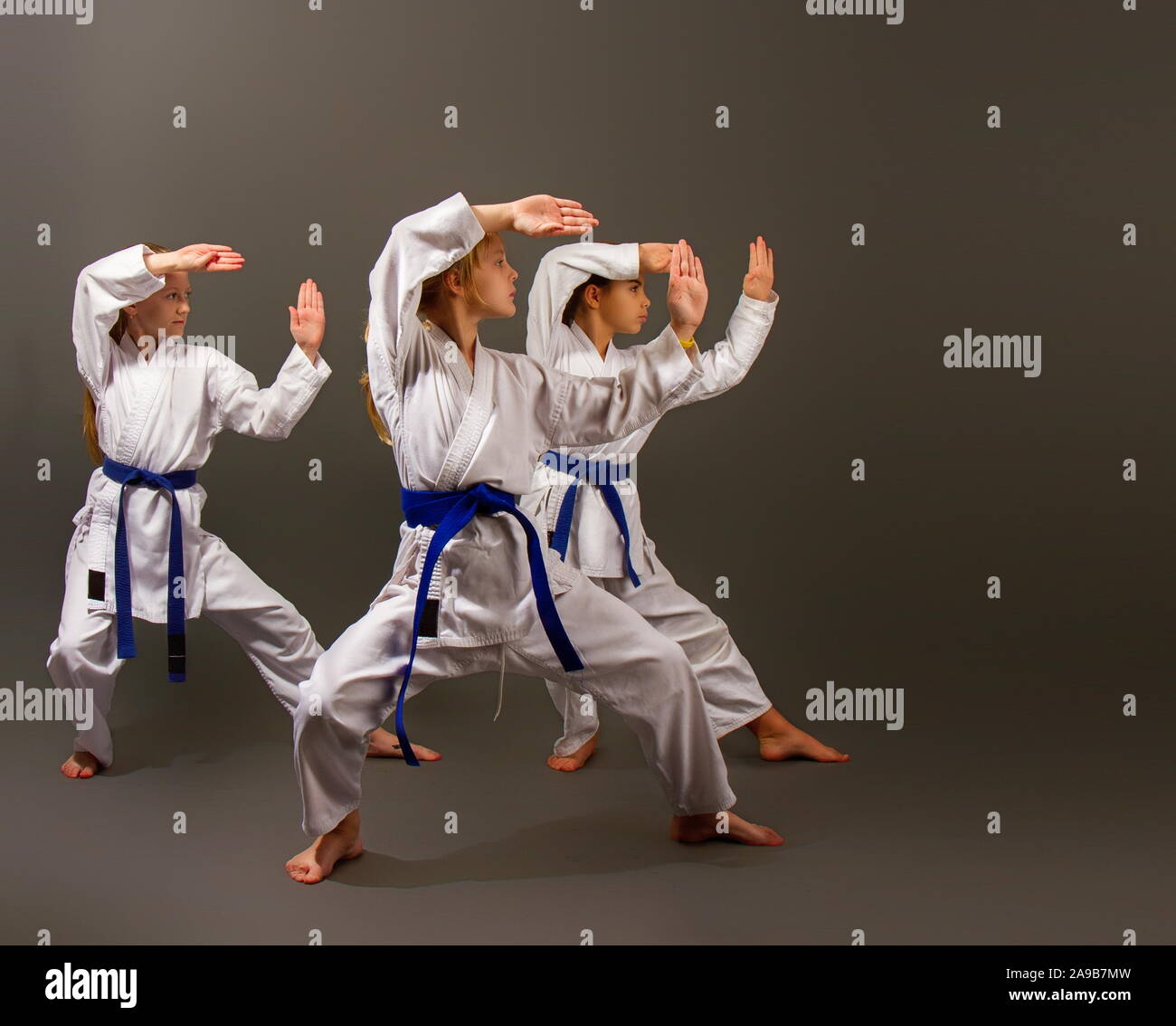 Drei kleine Karate Mädchen in einem weißen Kimono und Blaue Bänder führen Sie einen schönen Team kata auf einem dunklen Hintergrund Stockfoto
