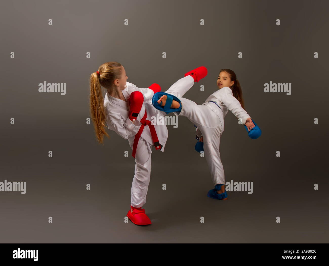 Zwei kleine Karate Mädchen in Kimonos und volle Sport Schutzausrüstung von roten und blauen Kampf gegen einen dunklen Hintergrund Stockfoto
