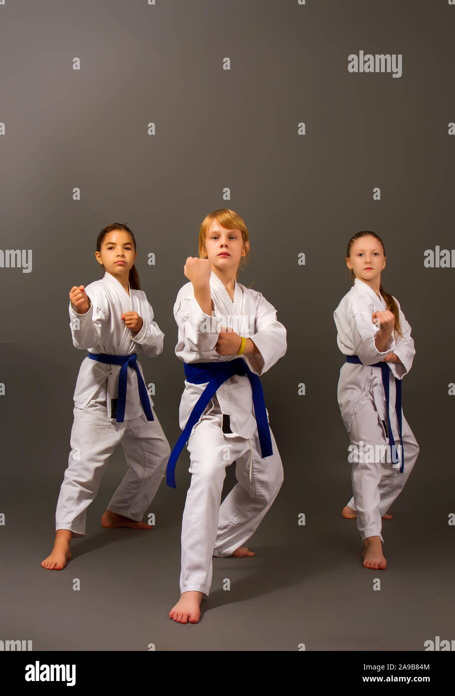 Drei kleine Karate Mädchen in einem weißen Kimono und Blaue Bänder führen Sie einen schönen Team kata auf einem dunklen Hintergrund Stockfoto