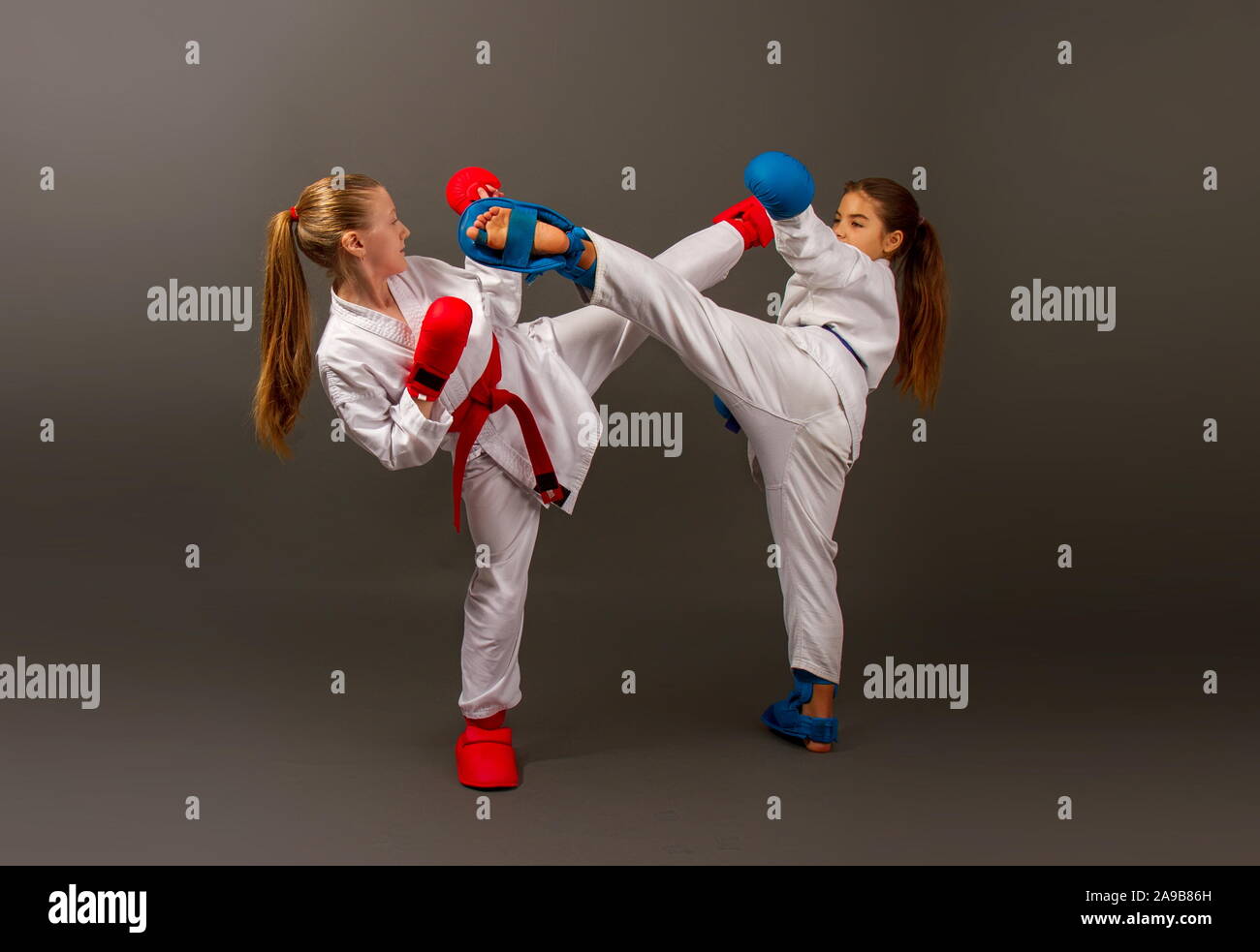 Zwei kleine Karate Mädchen in Kimonos und volle Sport Schutzausrüstung von roten und blauen Kampf gegen einen dunklen Hintergrund Stockfoto