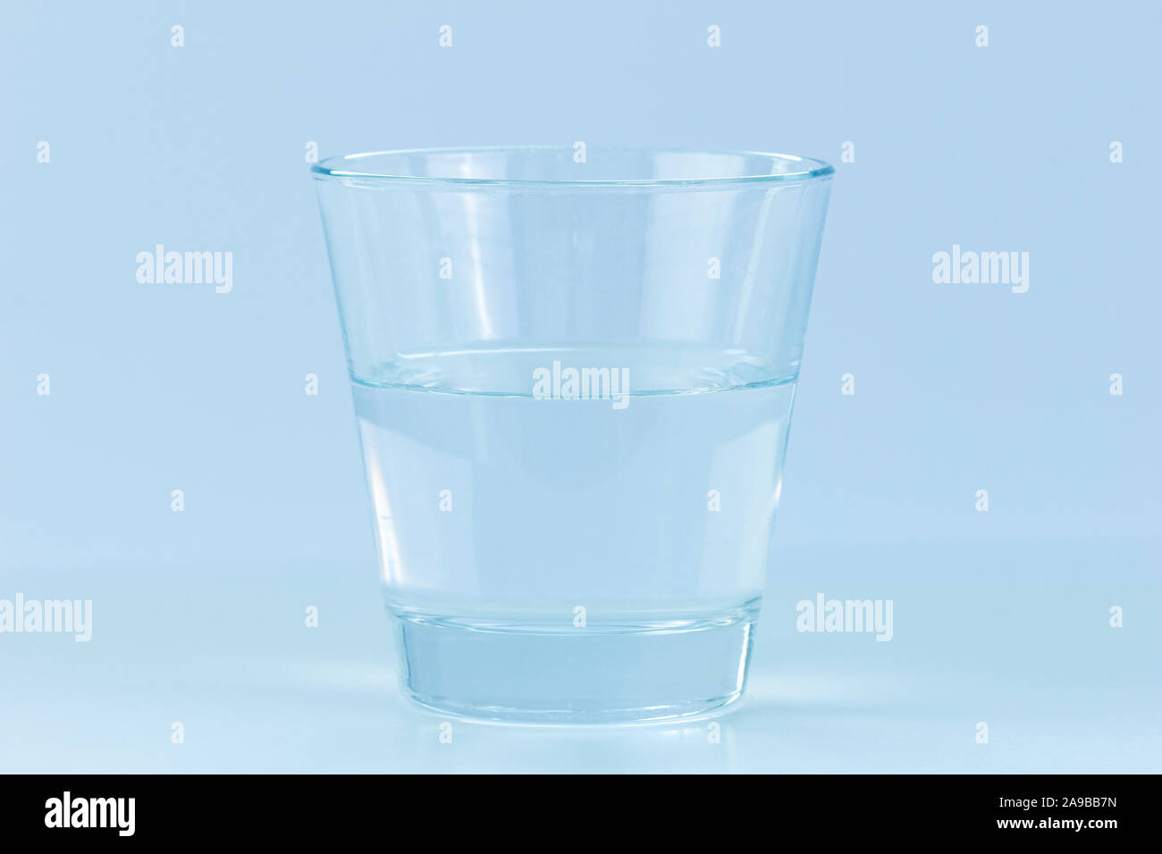 Nahaufnahme einer transparenten Glas halb voll oder leer. Konzept Foto von positive oder negative Haltung. Blauen Farbton. Stockfoto