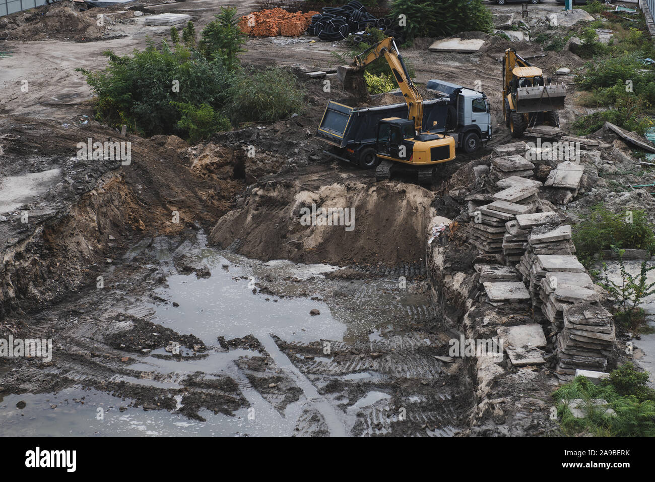 Bulldozer und LKW während der Arbeit. Bau eines neuen Gebäudes. Große Grube mit Wasser. Schlamm- und Baumaschinen. Blick von oben. Stockfoto