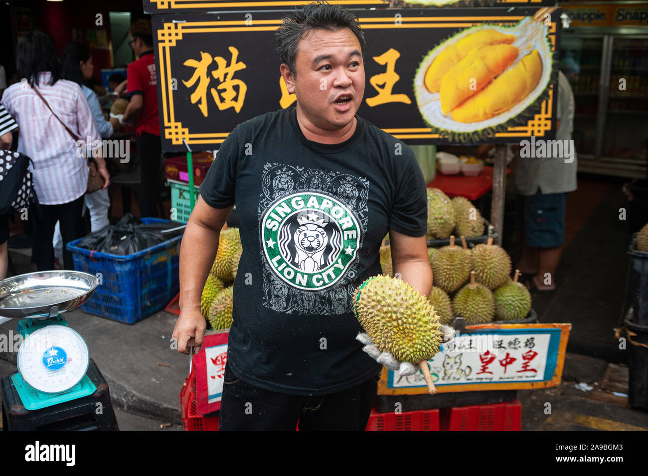 24.02.2019, Singapur, Singapur - ein Verkäufer eine frische Durian und ein Messer in der Hand auf einem Straßenmarkt in Chinatown. 0 SL 190224 D 033 CAROEX. Stockfoto