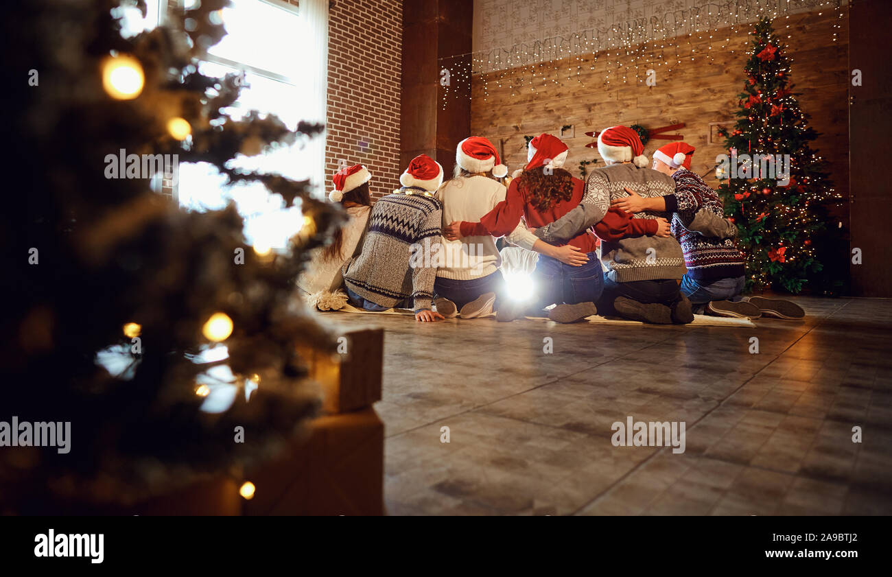 Zurück Blick auf erwachsene Männer und Frauen in Santa Hüte sitzen zusammen Hand in Hand angehoben Stockfoto