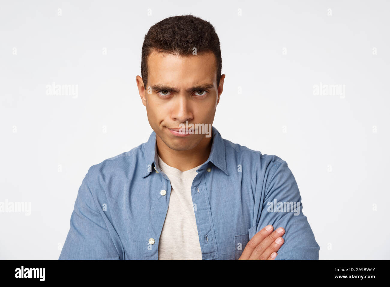 Wütend, enttäuscht und verärgert hübscher junger Mann, die Arme über der Brust unzufrieden, suchen unter Stirn judgmental, grinsen und Stare Stockfoto