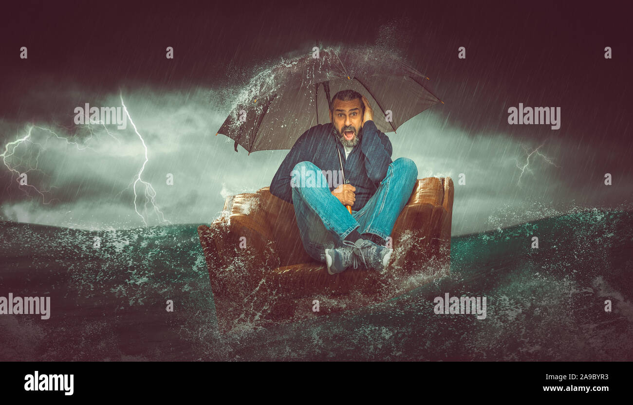 Der bärtige Mann sitzt auf einem Sessel in der Mitte des Meeres. Tierheim mit einem Regenschirm von einem Gewitter. Krise Konzept. Stockfoto