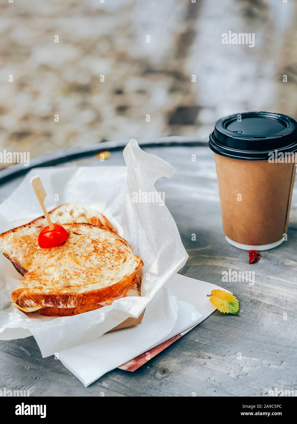 Panini mit Schinken und Käse sandwich Papier mit Kaffee Tasse auf einem hölzernen Tisch im Freien serviert. Street Market essen weg Konzept Stockfoto