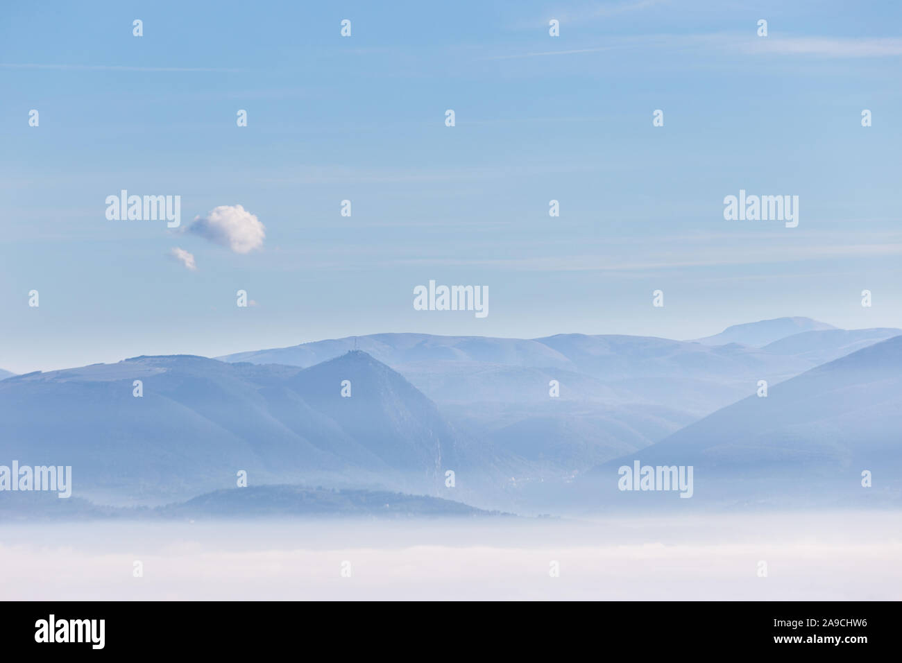 Nebel füllen ein Tal in Umbrien (Italien), mit Bergen und Hügeln unter einem blauen Himmel mit einem isolierten kleine Wolke Stockfoto