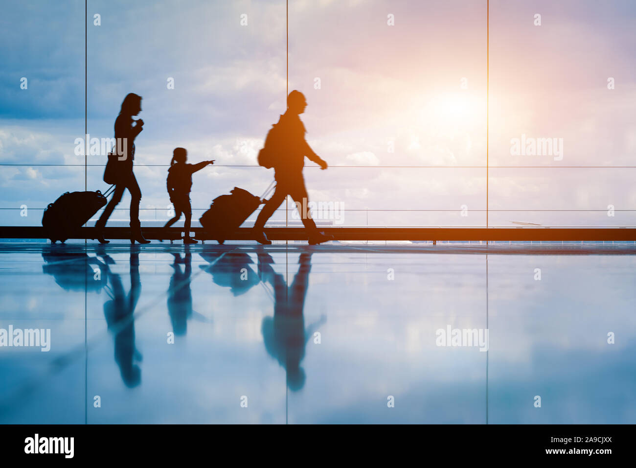 Familie am Flughafen Reisen mit kleinen Kindern und Gepäck zu Fuß zum Abflug-gate, Mädchen zeigen auf Flugzeuge durch Fenster, Silhouette von Menschen, Stockfoto
