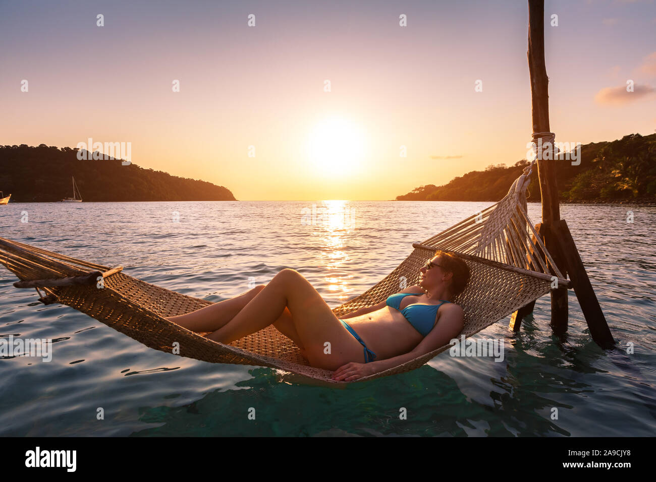 Frau am Strand in der Hängematte über Meer Wasser, warmen und sonnigen Sommer Abend in Urlaub Ferien Hotel, glücklichen Moment bei Sonnenuntergang Stockfoto