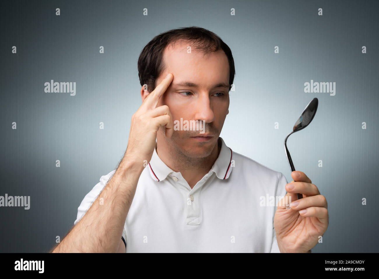 Porträt eines Mannes mit telekinetischen Kräfte Holding Edelstahl Löffel gegen grauer Hintergrund Stockfoto