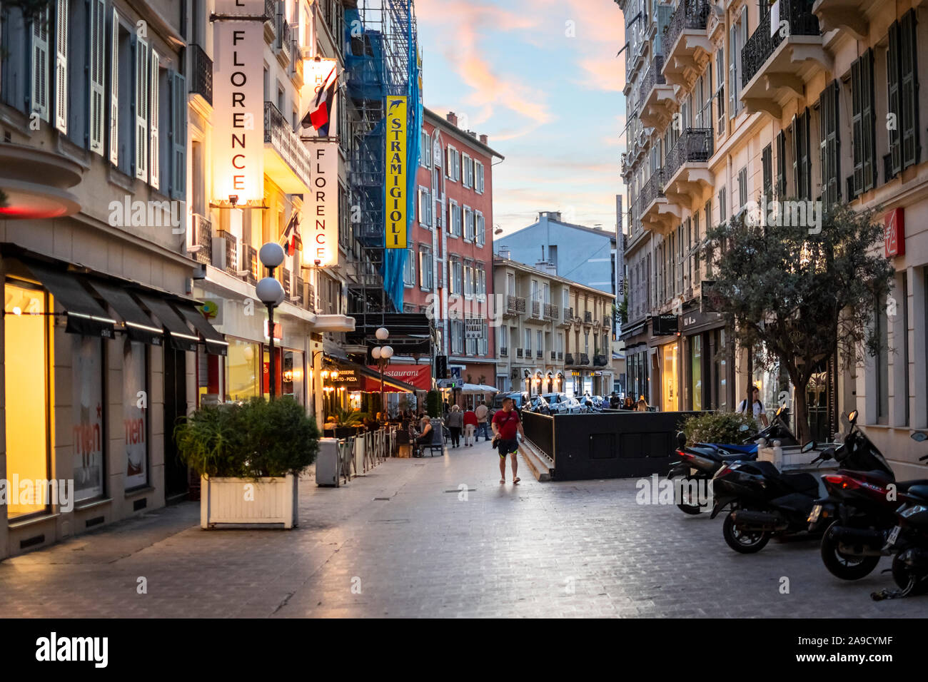 Am frühen Abend in der Stadt von Nizza Frankreich als Fußgänger und Einheimische in einem Straßencafé mit einem bunten Sonne hinter Set speisen. Stockfoto