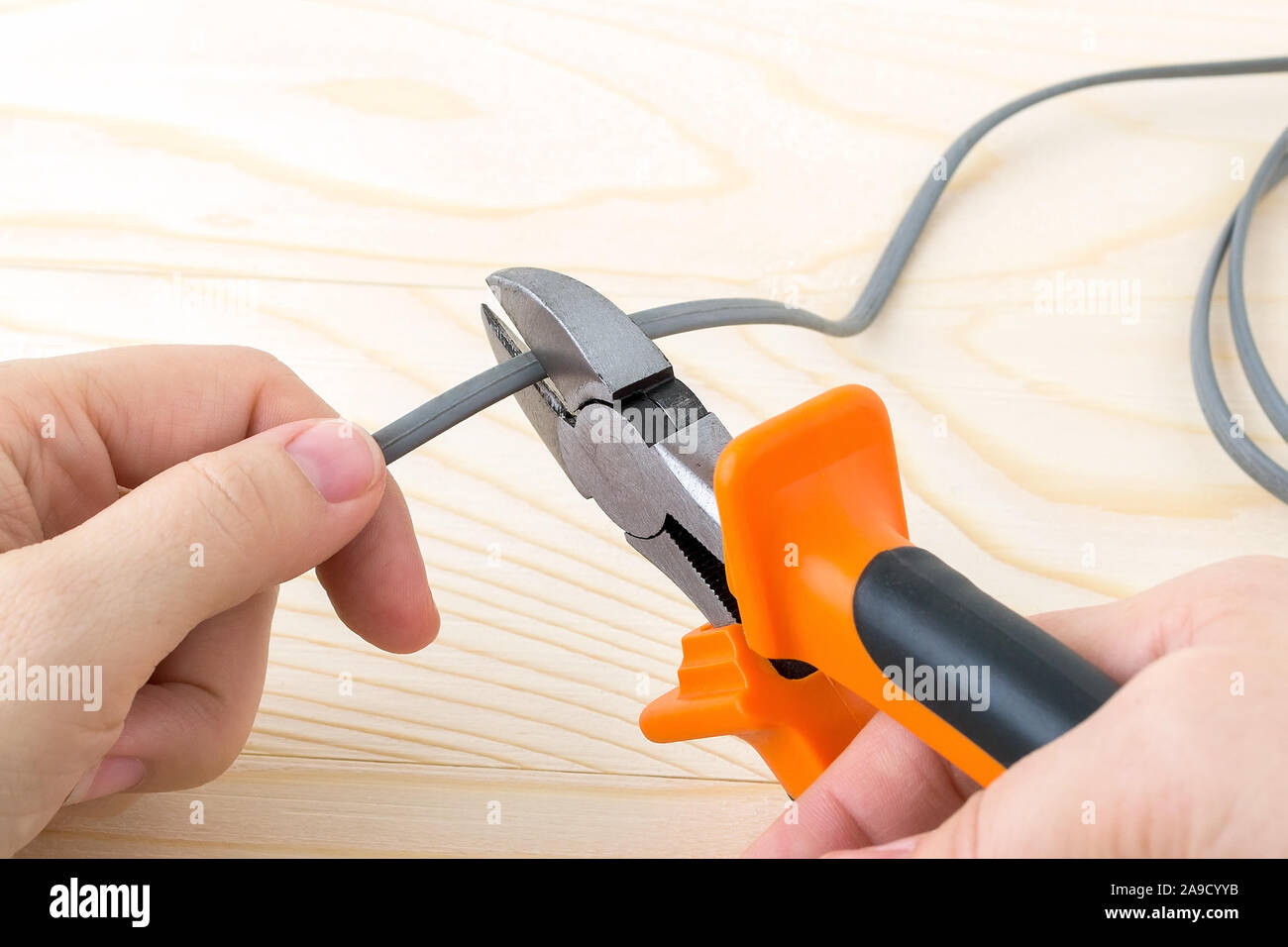 Frau Hand holdins ein Metall Seitenschneider mit orange schwarz gummierte  Griffe und Schneiden einen Draht über eine raue Holz- Hintergrund.  Elektriker Werkzeug Stockfotografie - Alamy