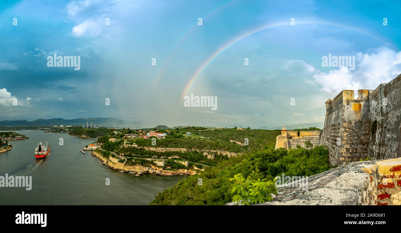 Doppelter Regenbogen über San Pedro De La Roca Burgmauern Panorama und Bucht mit Frachtschiff, Santiago de Cuba, Kuba Stockfoto