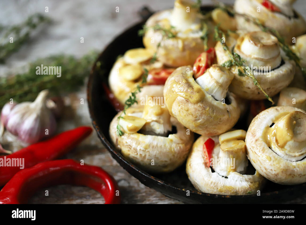 Große rohe Champignon-Pilze in einer Pfanne. Pilze in Sauce vor dem Backen. Vegane Küche. Rohe Champignons in Sauce mit Thymian mariniert Stockfoto