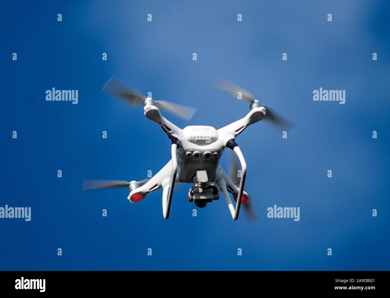 Weiße Drohne am blauen Himmel mit sich drehenden Propellern. Stockfoto