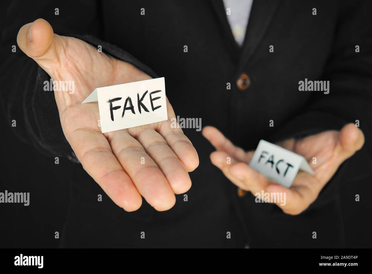 Ein Stück Papier mit der Aufschrift fake in die Hand eines Mannes auf dem Hintergrund eines anderen Hand mit der Inschrift. Das Konzept der Täuschung und m Stockfoto
