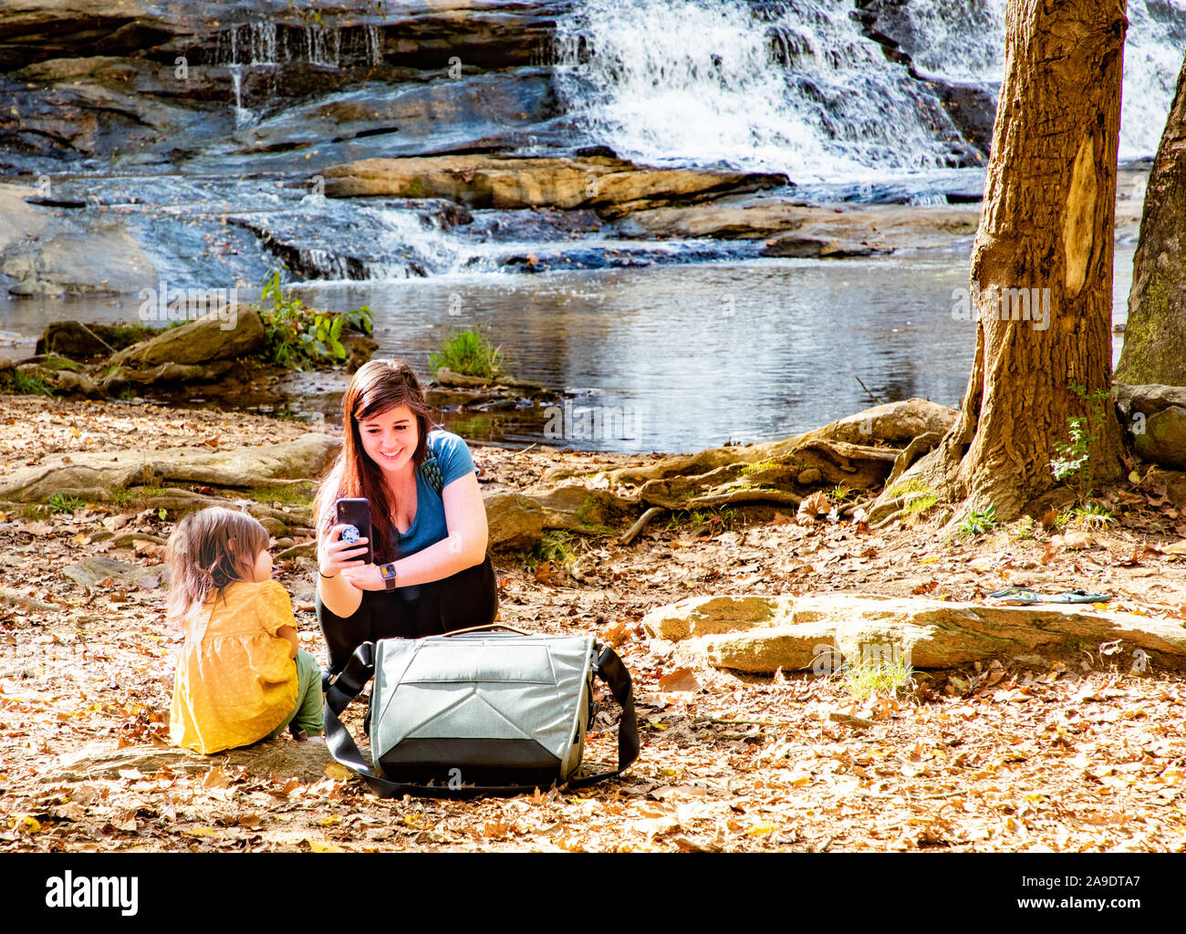 Mama, die Tochter auf dem Handy mit einem Wasserfall im Hintergrund fotografiert Stockfoto