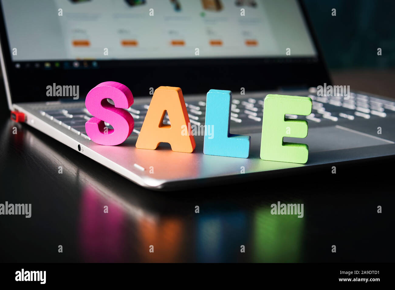 Große bunte Buchstaben Verkauf auf Laptop. Verkauf im online Shop Konzept. Geöffnet Notebook mit Holz- wort Verkauf auf der Tastatur über schwarzen Tisch. Internet Shop Stockfoto