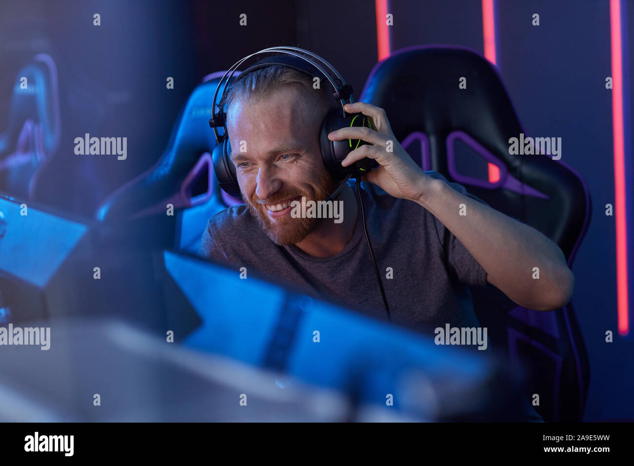 Happy bärtige junge Gamer in Kopfhörer am Computer Monitor schauen und Lachen im dunklen Zimmer sitzen Stockfoto