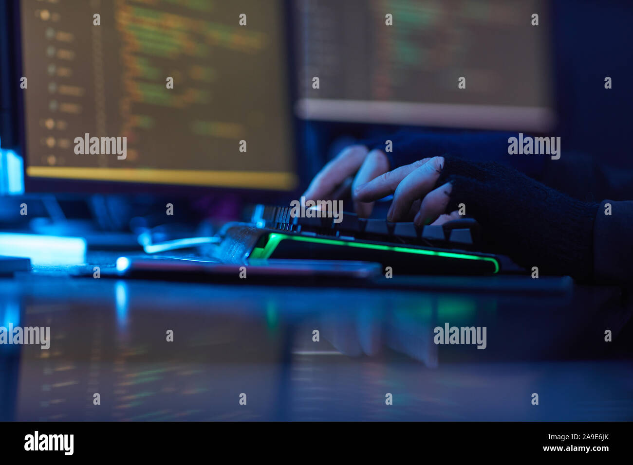 Nahaufnahme der Mann mit schwarzen Handschuhen Tippen auf der Computertastatur am Tisch in dunklen Büro Stockfoto
