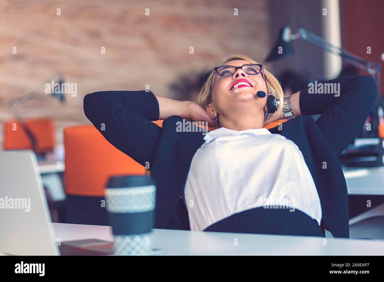 Attraktive Blondine im Büro am Schreibtisch entspannt. Die junge Frau lehnte sich in ihrem Stuhl beim Stillstehen. Stockfoto