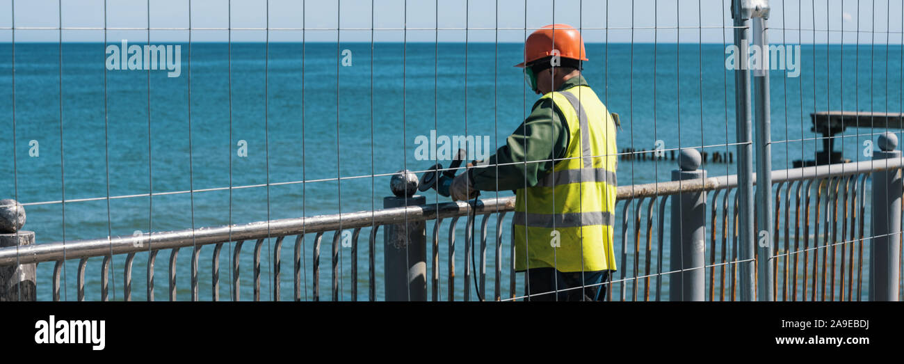 Arbeiter mit Winkelschleifer. Die Arbeit an der Wiederherstellung der Böschung Zaun. 2019-05-30. Kaliningrad, Russland Stockfoto