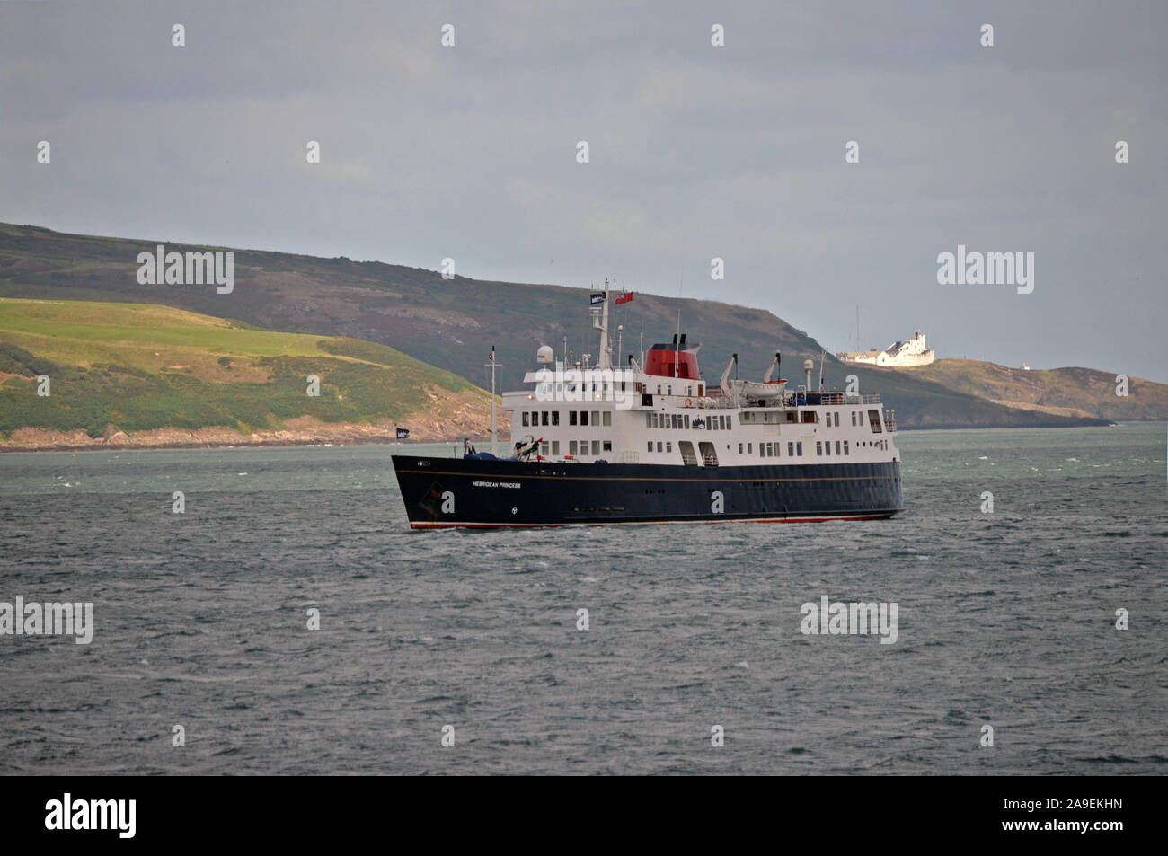 HEBRIDEAN PRINCESS wiegt Anker in DULAS BAY vor ANGLESEY mit POINT LYNAS Leuchtturm jenseits Stockfoto