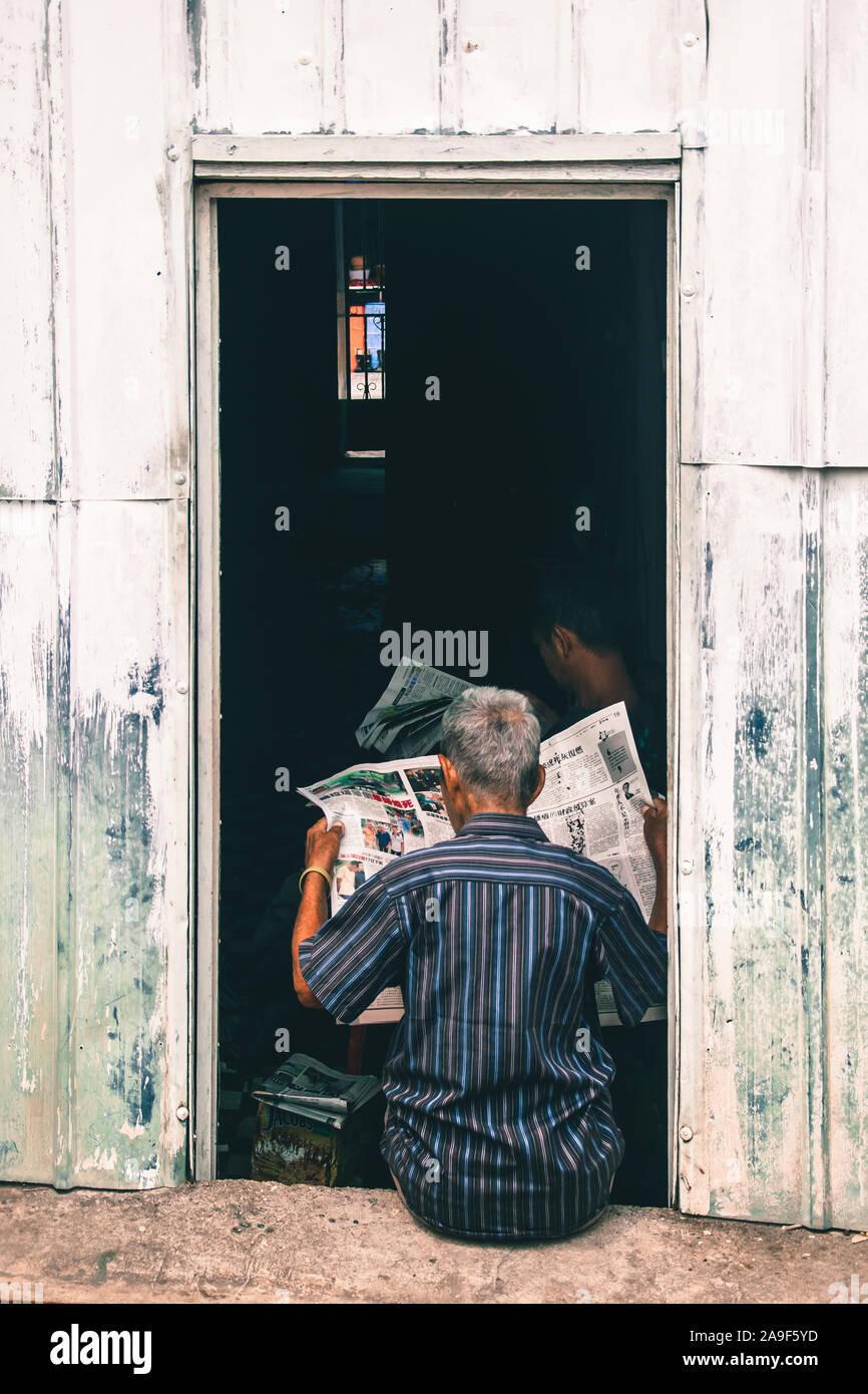 Malaysische alter Mann Lesen seiner chinesischen Zeitungen vor der Haustür Stockfoto