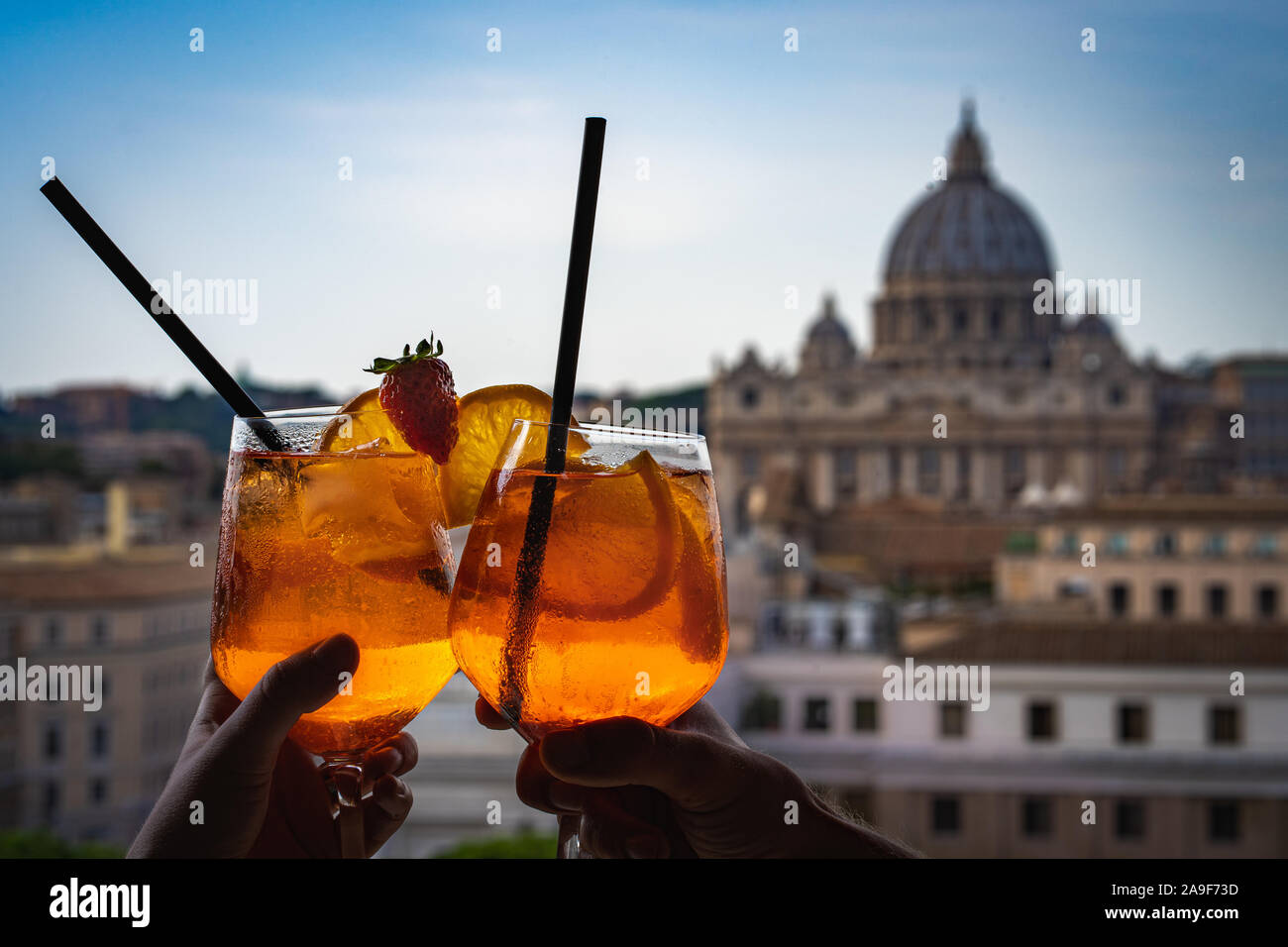 Ein paar hält Gläser Aperol in der Bar im Inneren der Burg Sant'Angelo. Gläser Aperol und Petersdom im Hintergrund. Stockfoto