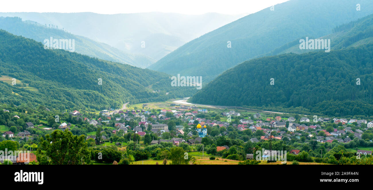Panoramablick auf das Tal mit dem kleinen Dorf zwischen Bergen Stockfoto Panoramablick auf das Tal mit dem kleinen Dorf zwischen Bergen Stockfoto