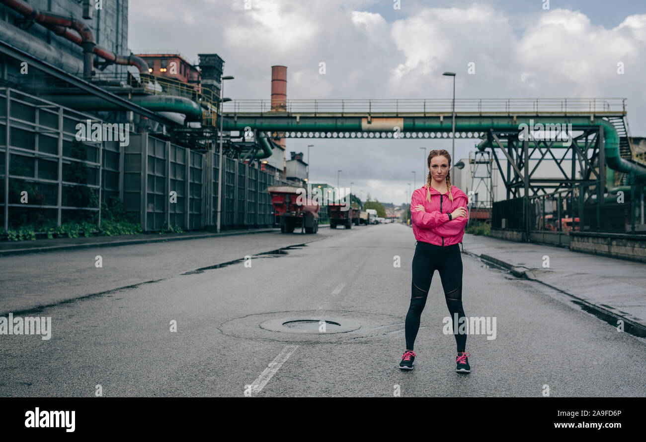Sportlerin, die Arme in einem Industriegebiet gekreuzt Stockfoto