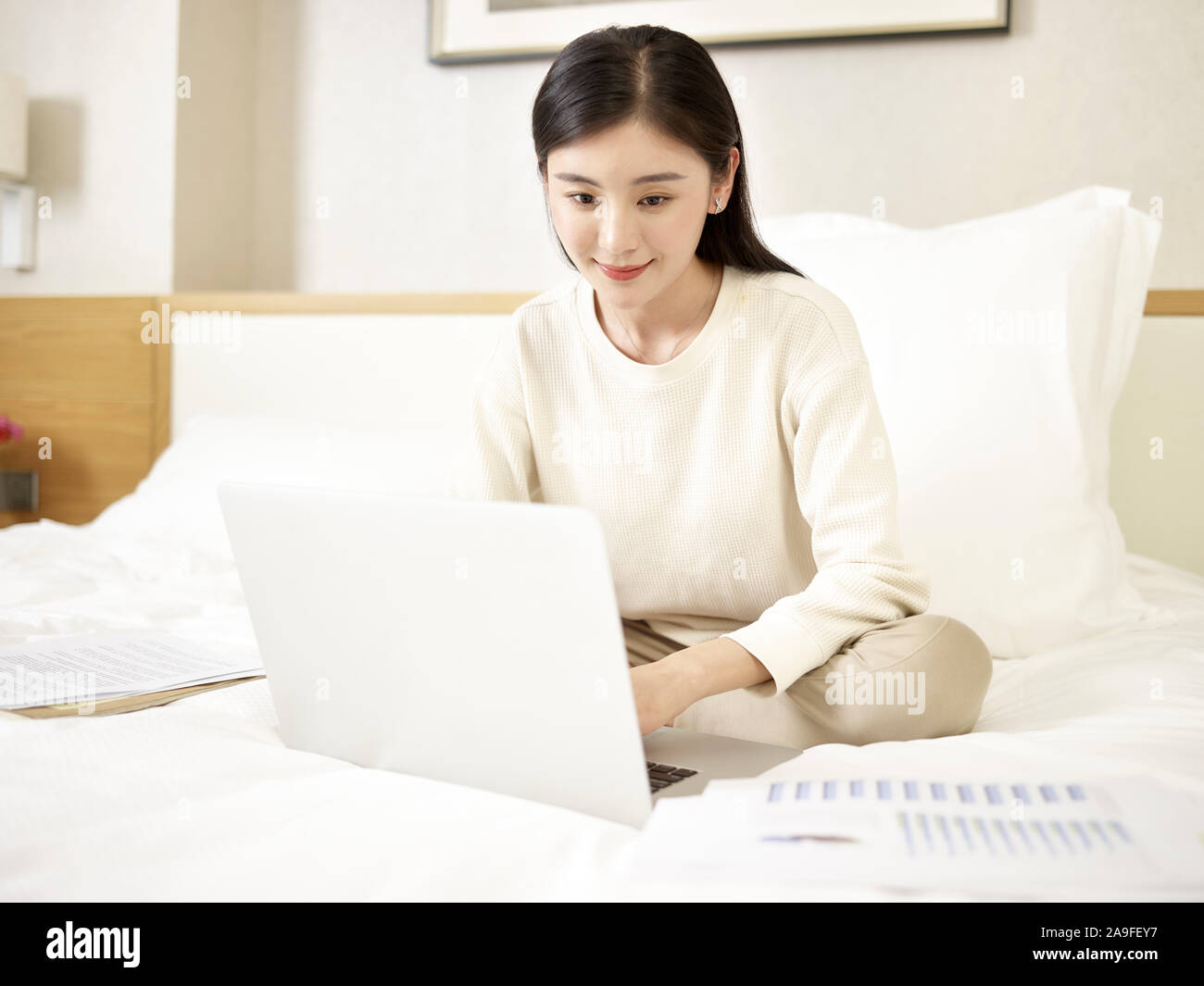 Schöne junge asiatische Frau sitzt auf dem Bett arbeiten mit Laptop Stockfoto
