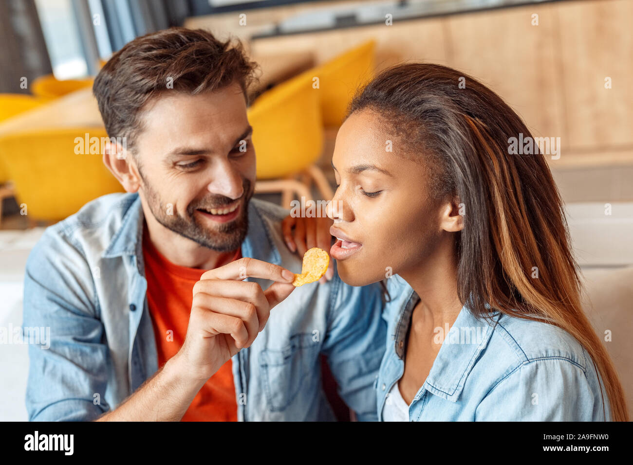 Junge erwachsene Frau und Mann essen Chips zu Hause Stockfoto