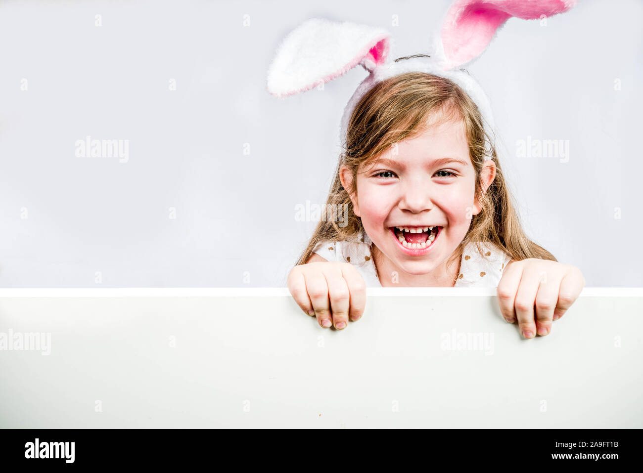 Gerne süßes Kind Mädchen in einem Hase Kostüm mit Hase Ohren mit einem Korb von bemalte Eier Einblicke hinter der Wand. Ostern Konzept. Hintergrund Stockfoto