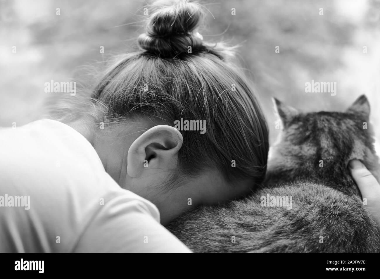 Trauriges Mädchen mit Katze sitzt mit dem Rücken zur Kamera. Das Mädchen lehnte ihren Kopf gegen die Katze. beleidigt Kind. Schwarz/Weiß-Bild horizontal. Stockfoto