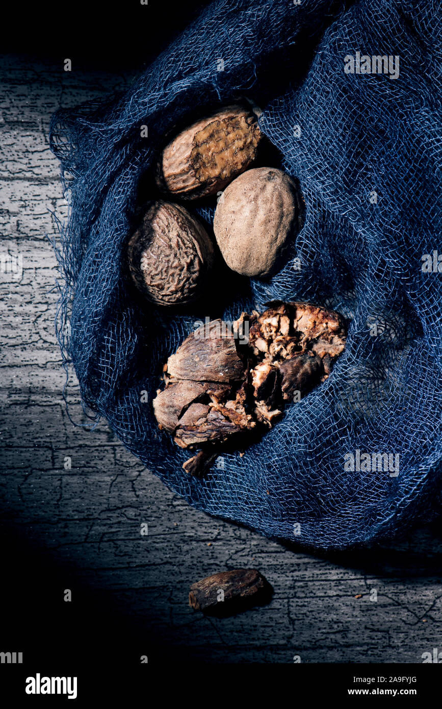 Nahaufnahme von einigen geschält und getrocknet Muskatnuss Samen in einem dunklen Grau gaze Stoff, auf einem grauen Holztisch leicht beleuchtet Stockfoto
