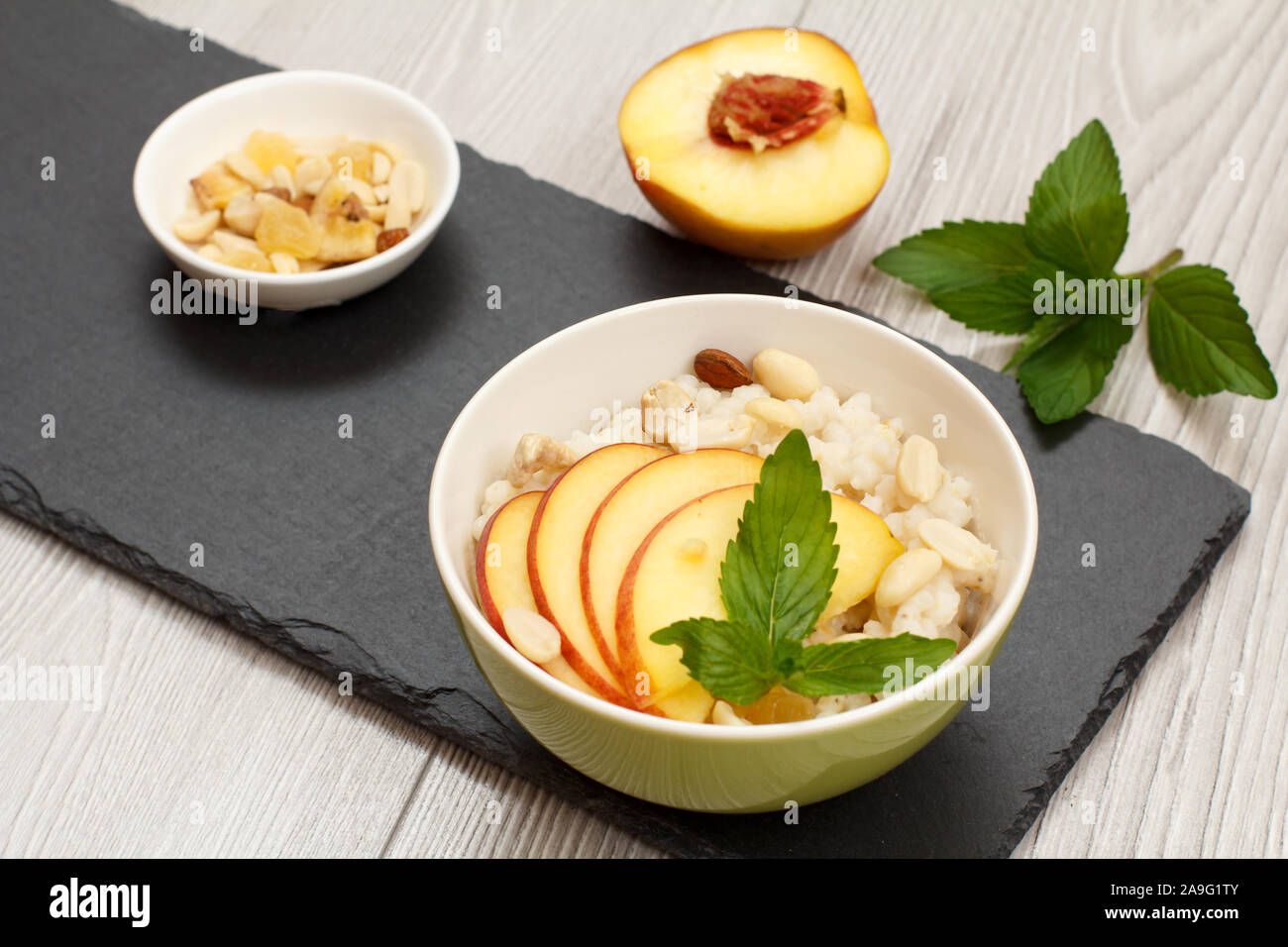 Porzellan Schüsseln mit sorghum Porridge, Pfirsich, Cashewnüsse, Mandel- und Minze auf Stein. Vegan glutenfrei Hirse Salat mit frischen Früchten. T Stockfoto