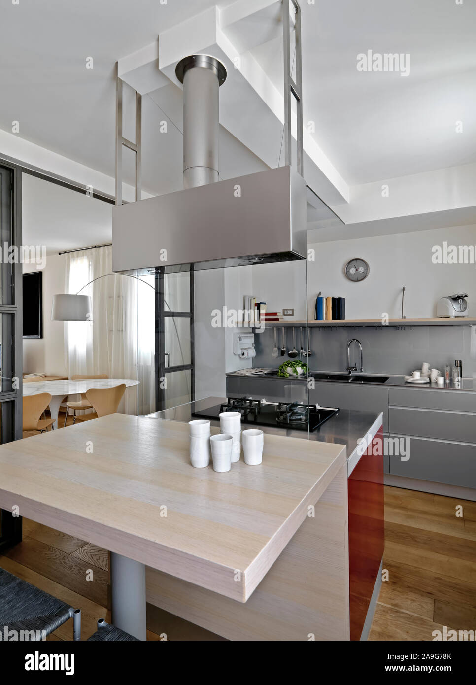 Innere Aufnahme einer modernen Küche im Vordergrund der Küche mit Esstisch und einem Gasherd, während im Hintergrund die Küchenschränke mit Bu Stockfoto