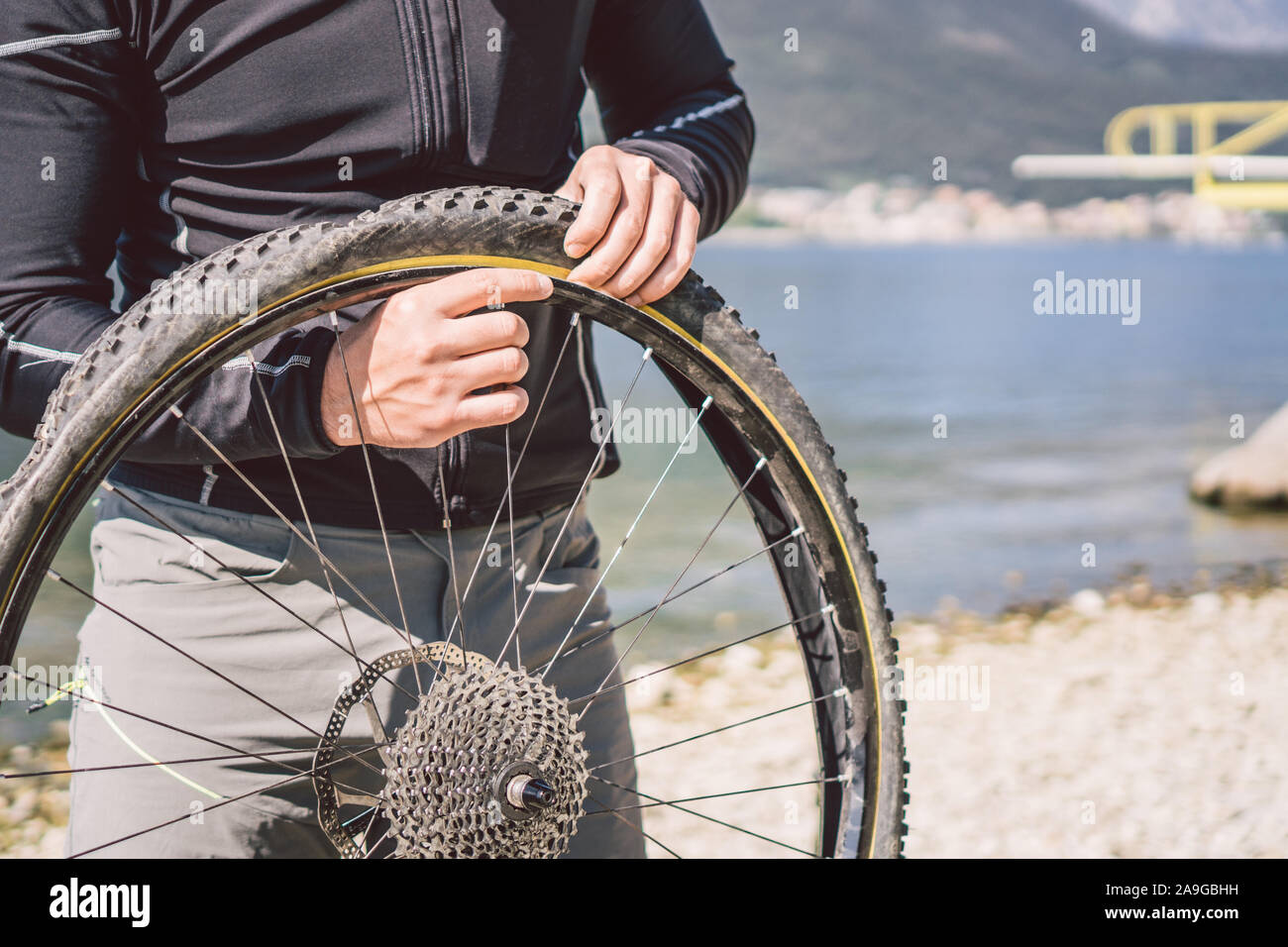 Fahrrad reparieren. Mann Instandsetzung Mountainbike. Radfahrer Mann in Schwierigkeiten hinten Wheel bei Unfall. Mann Bike in der Nähe von See in Italien Hintergrund Stockfoto