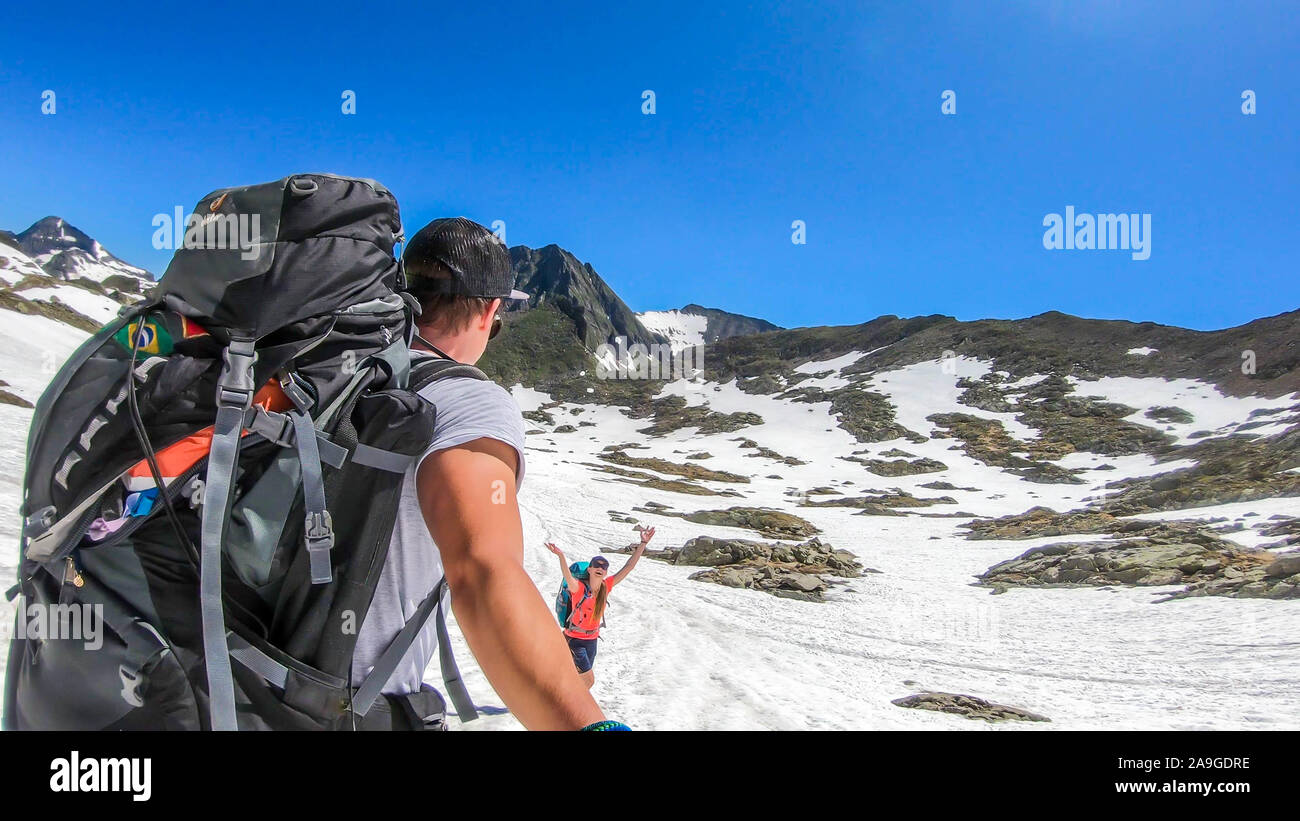 Ein paar mit großen Rucksäcken Spaziergänge auf den schneebedeckten Hang in den hohen Bergen. Schladming Alpen, Österreich. Das Mädchen ist um springen, glücklich zu sein. Der Mensch ist Taki Stockfoto