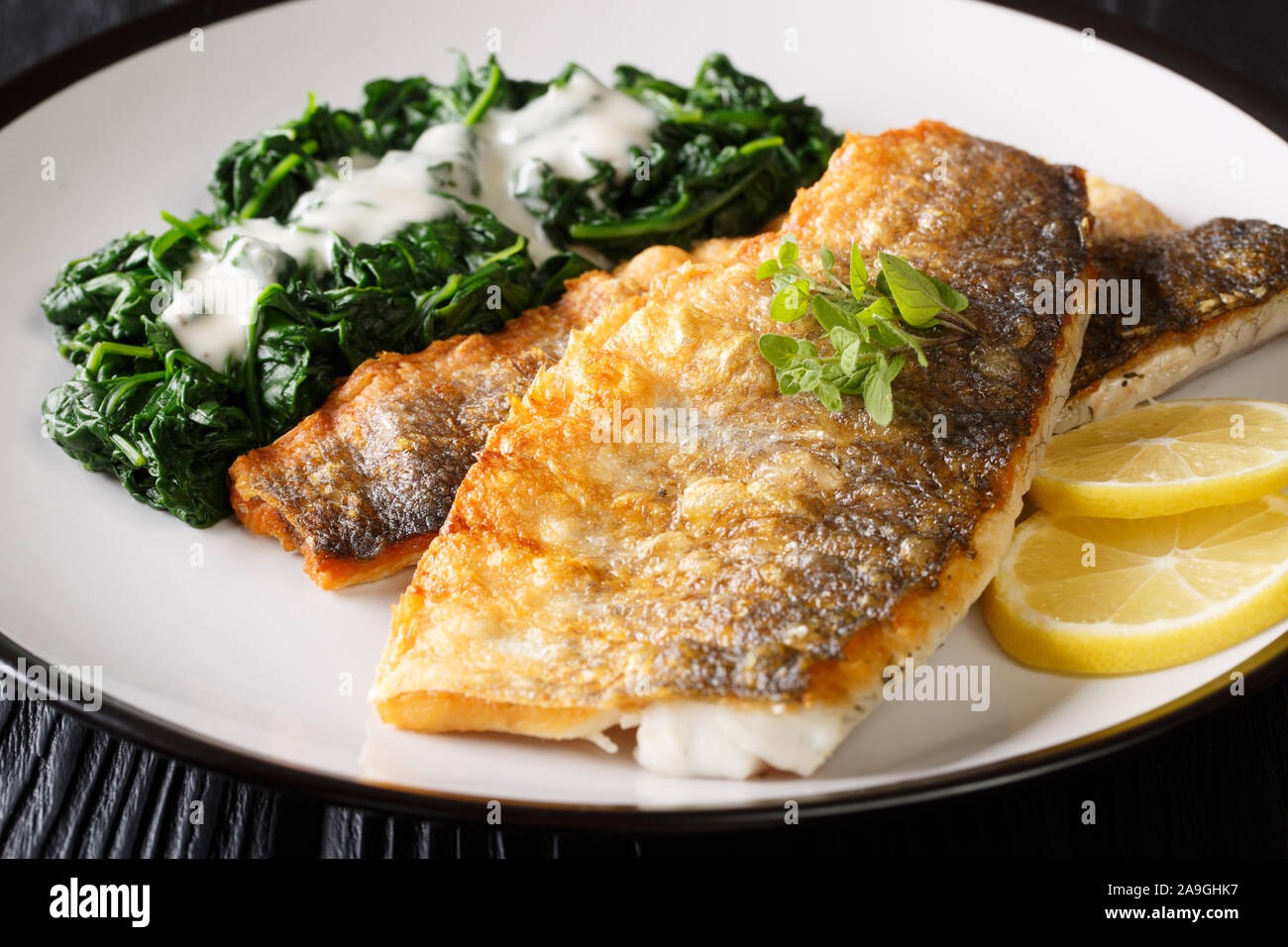 Lecker gegrilltes Barschfilet mit Spinat und Zitrone close-up auf einem Teller auf den Tisch. Horizontale Stockfoto