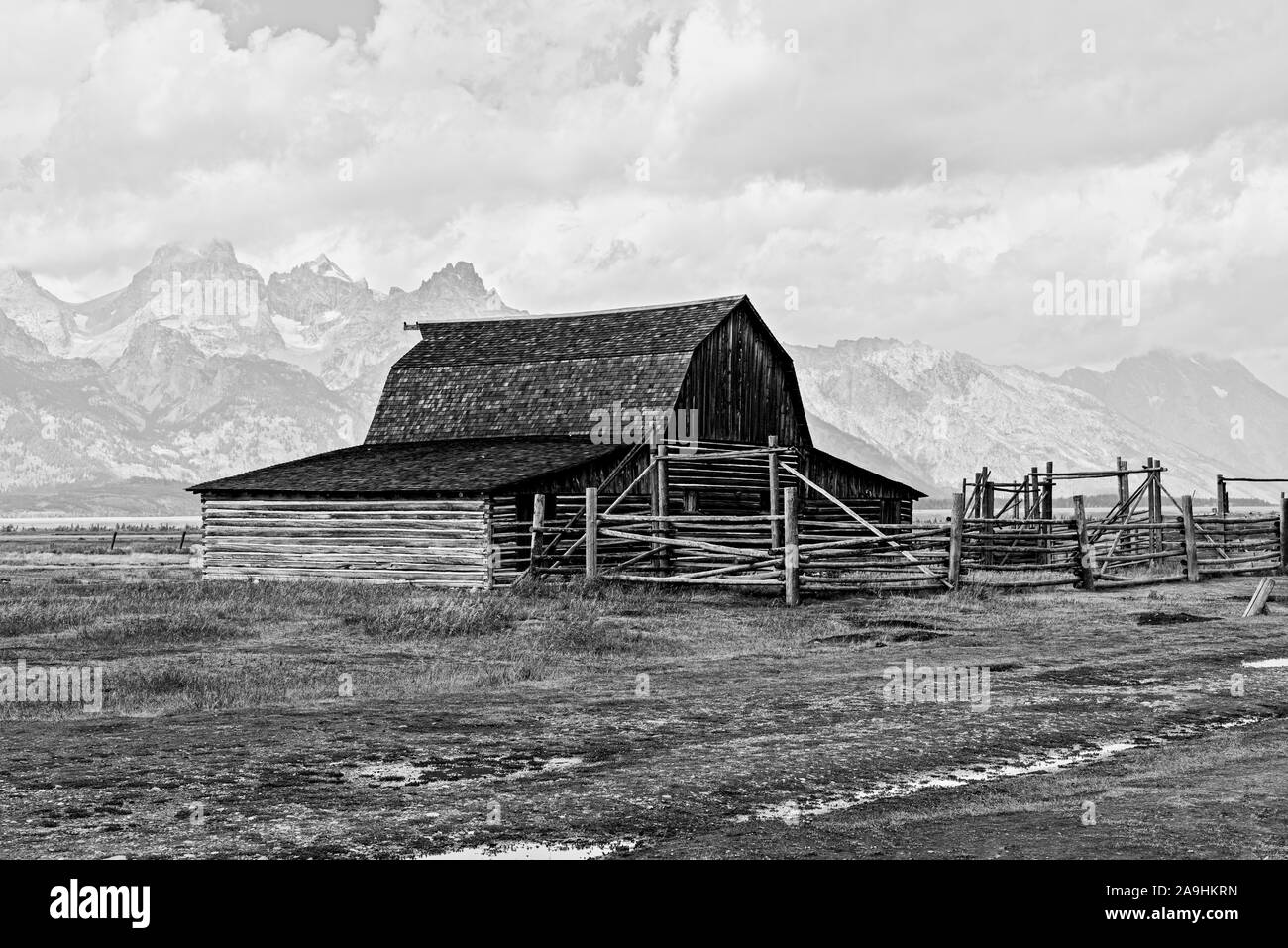 Alte Scheune auf dem Land mit hohen Rocky Mountains im Hintergrund unter bewölktem Himmel, schwarz und weiß. Stockfoto